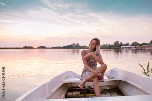 Girl in a dress sitting on the boat and enjoying in a beautiful sunset while drinking beer © Jovica Varga