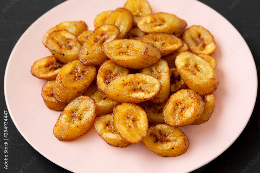 Homemade fried plantains on a pink plate on a black backgound, low angle view. Closeup. Homemade fried plantains on a pink plate on a black backgound, low angle view. Closeup.