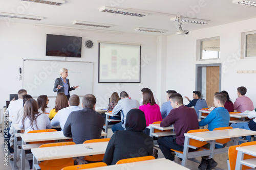Female attractive professor explain lesson to students and interact with them in the classroom.Helping a students during class. University student being helped by female lecturer during class.