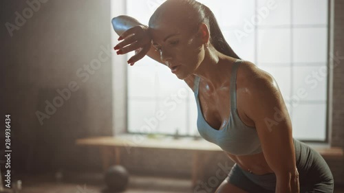 Portrait of a Beautiful Strong Fit Brunette Wiping Sweat from Her Face in a Loft Industrial Gym with Motivational Posters. She's Catching Her Breath after Intense Fitness Training Workout. Warm Light. photo