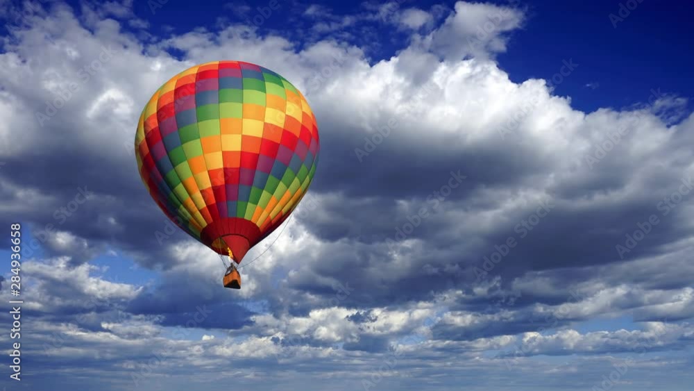 A colorful hot air balloon coming closer against a fluffy clouds time lapse sky. A colorful hot air balloon coming closer against a fluffy clouds time lapse sky.