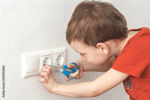 Little boy plays with electric socket and scissors. High voltage hazard