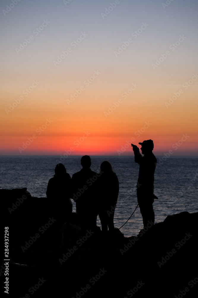 A silhouette of people standing on the waterfront during a sunrise over the water