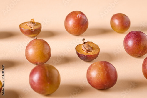 Pattern, texture of sliced half ripe sweet plum fruits with water drops on cream colored background, bright, angle view