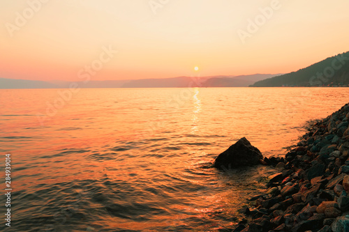Picturesque sunset in golden orange colors on a rocky beach, late summer evening