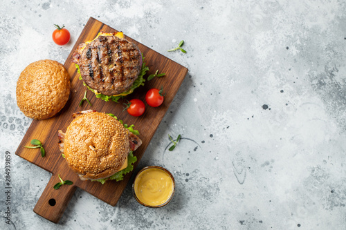 Tasty grilled home made burger with beef, tomato, cheese, bacon and lettuce on a light stone background with copy space. Top view. fast food and junk food concept. Flat lay photo