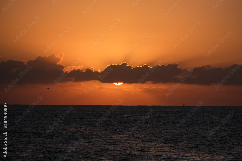 Sunrise over the ocean with an orange sky and some birds