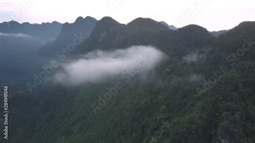 clouds and green thick rain forest cover high steep dark mountain range under gray sky bird eye view photo