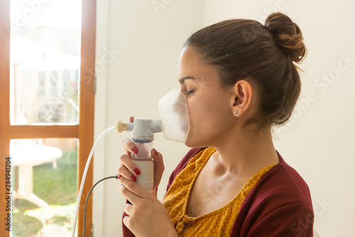 Young woman doing inhalation nebulizer in hospital, holding a mask nebuliser inhaling asthma and bronchitis medication to improve breathing. Healthcare, medicine, disease concept. photo