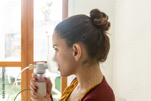 Young woman doing inhalation nebulizer in hospital, holding a mask nebuliser inhaling asthma and bronchitis medication to improve breathing. Healthcare, medicine, disease concept. photo