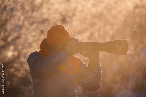 A photographer with a camera and a telephoto lens shoots on a frosty winter morning. Lebedinyj Swan Nature Reserve, Svetloye lake, Urozhaynoye Village, Sovetsky District