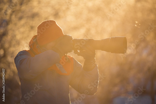 A photographer with a camera and a telephoto lens shoots on a frosty winter morning. Lebedinyj Swan Nature Reserve, Svetloye lake, Urozhaynoye Village, Sovetsky District photo