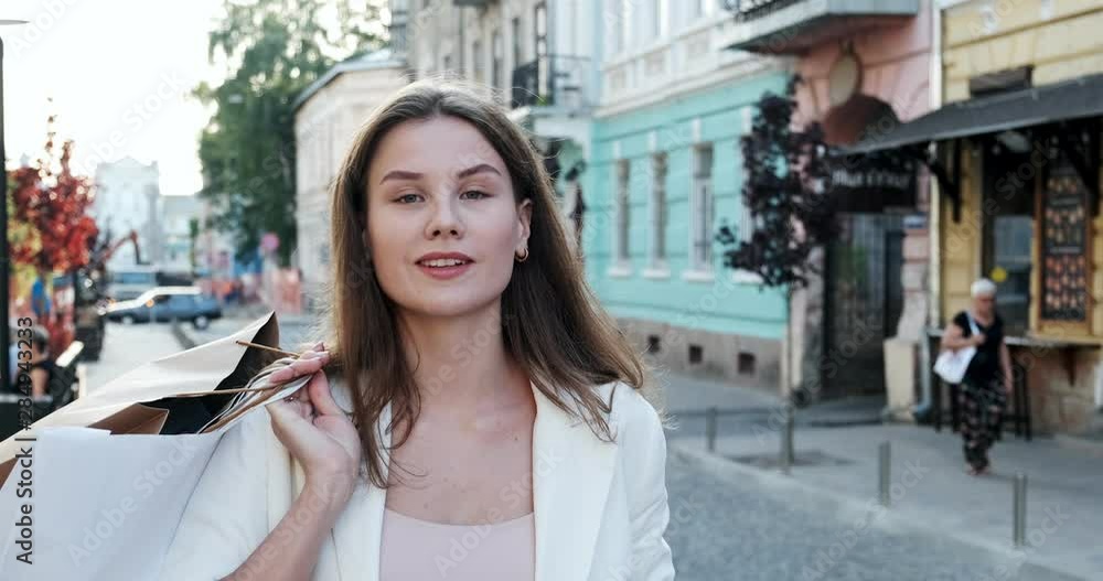 Happy, smiling, beautiful, young woman walks through the city on shopping with purchases in the period sales