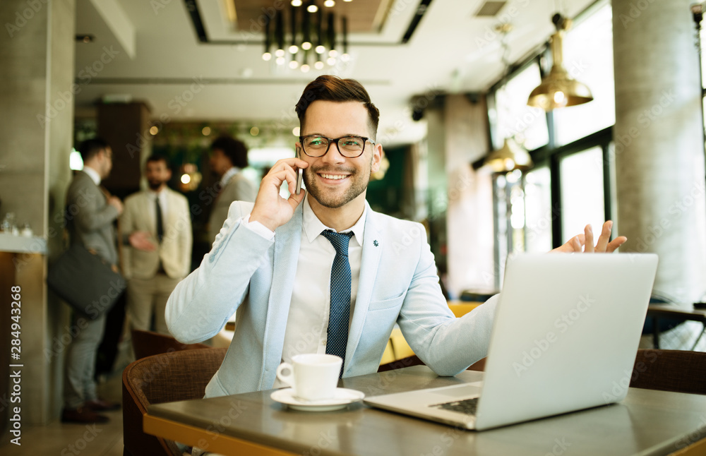 Young businessman uses a laptop in a cafe and talking mobile Young businessman uses a laptop in a cafe and talking mobile