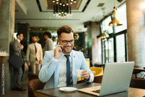 Young businessman uses a laptop in a cafe and talking mobile