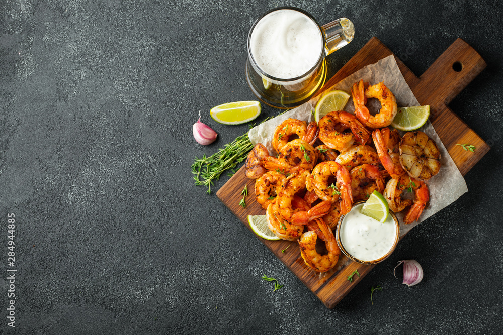 Grilled shrimps or prawns served with lime, garlic and white sauce on a dark concrete background. Seafood. Top view with copy space. Flat lay - obrazy, fototapety, plakaty 