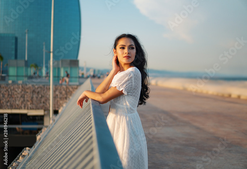 Beautiful smiling girl in the white dress walking along the sea promenade. Elegance and tenderness concept