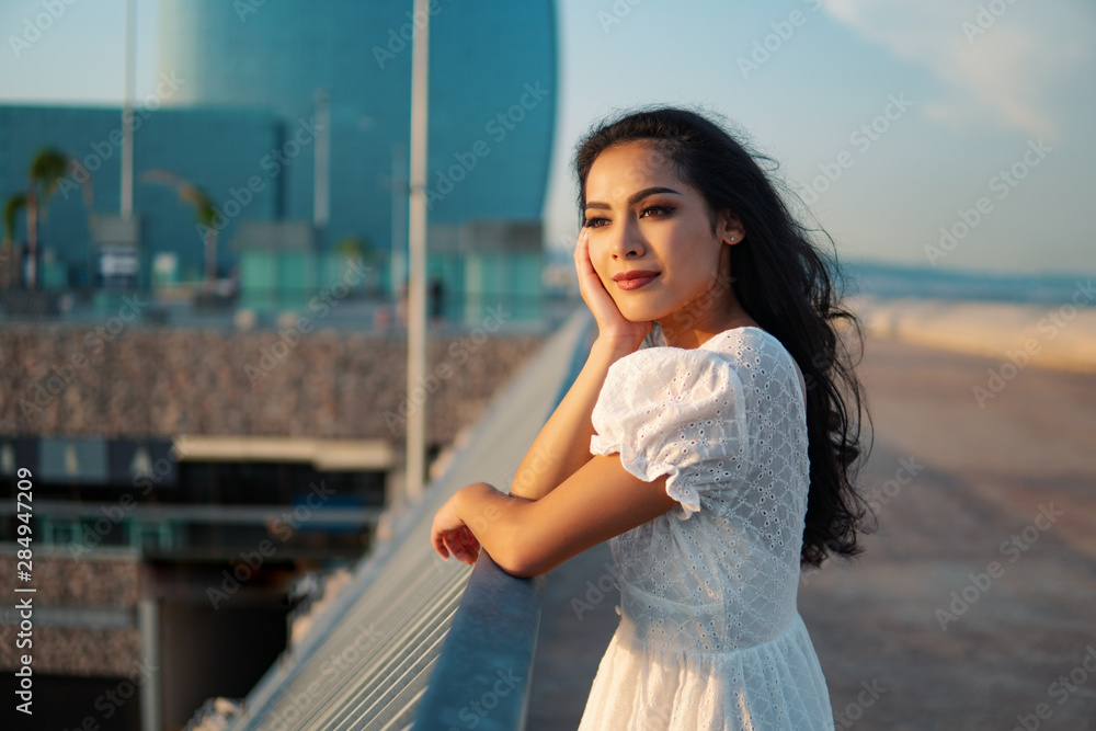 Beautiful girl in the white dress waiting along the sea promenade. Elegance and tenderness concept Beautiful girl in the white dress waiting along the sea promenade. Elegance and tenderness concept