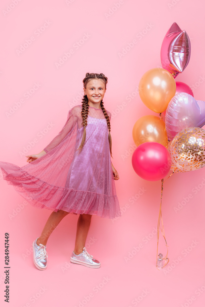 Happy and beautiful teen girl holding a bunch of colorful balloons and looking at camera with smile on pink background Happy and beautiful teen girl holding a bunch of colorful balloons and looking at camera with smile on pink background