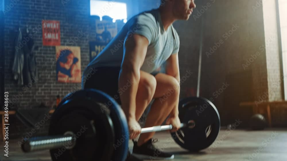 Handsome Muscular Man Does Overhead Deadlift with a Barbell in a Small Authentic Gym. Athletic Man Training His Arm Muscles and Exercises with Barbell. Workout in the Hardcore Gym. Warm Light. Handsome Muscular Man Does Overhead Deadlift with a Barbell in a Small Authentic Gym. Athletic Man Training His Arm Muscles and Exercises with Barbell. Workout in the Hardcore Gym. Warm Light.