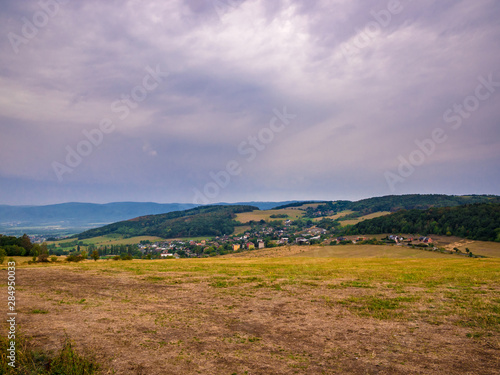 Landscape with dry meadows, forest, village in the valley and cloudy sky