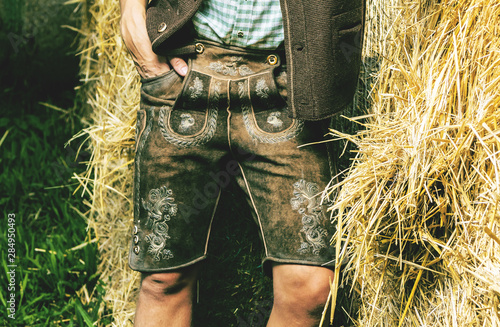Fotografie Mann in bayerischen lederhosen steht vor einem strohballen