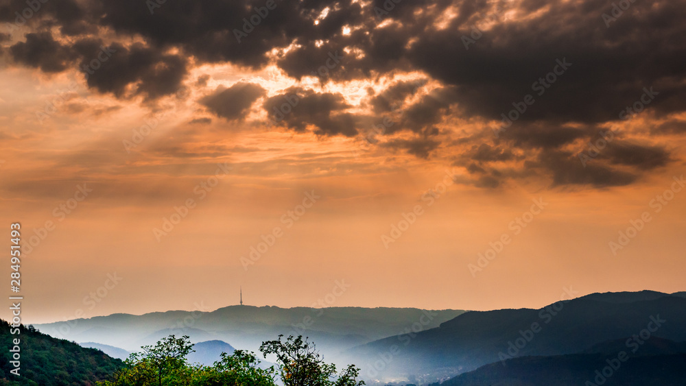 Naklejka premium Dark morning clouds with sun rays and mist in the valley - on the horizon is the outline of the radio tower