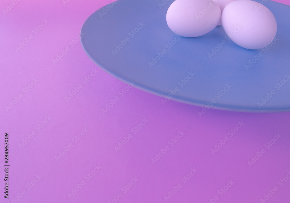 A light blue neutral plate with white chicken eggs on a neutral pink background. Free space to write. A light blue neutral plate with white chicken eggs on a neutral pink background. Free space to write.
