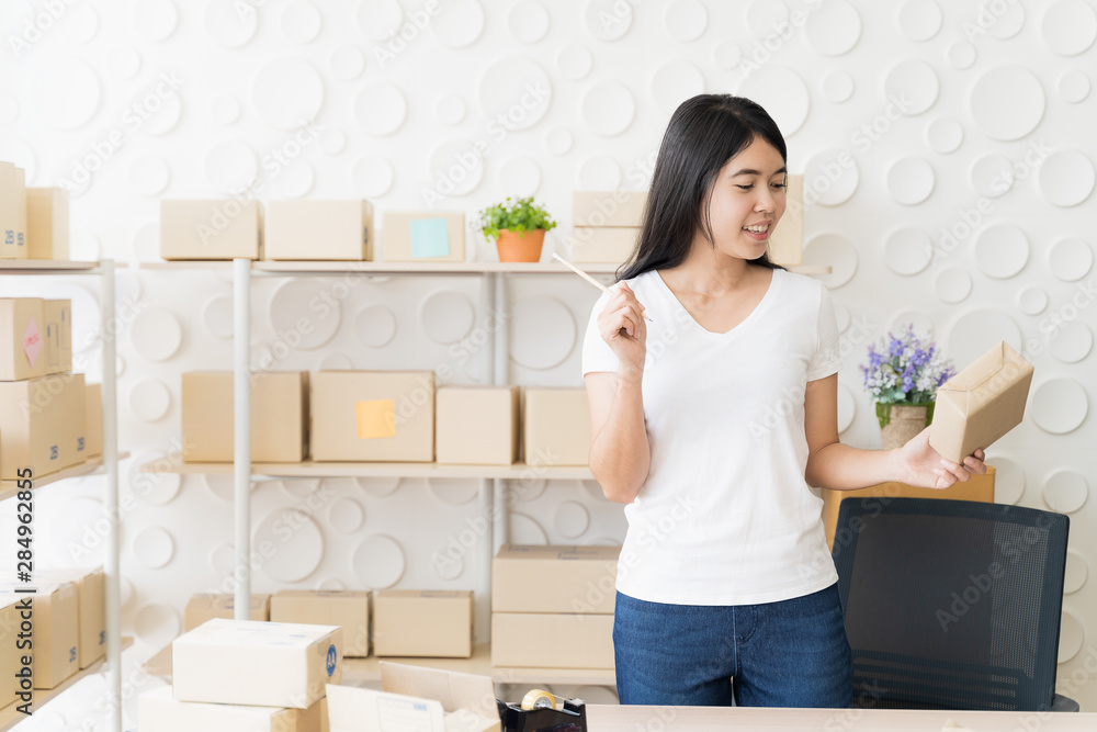 Asian freelance woman working at home and start up small business entrepreneur SME with internet online. woman is preparing the goods in the package box to prepare the delivery for the customer.
