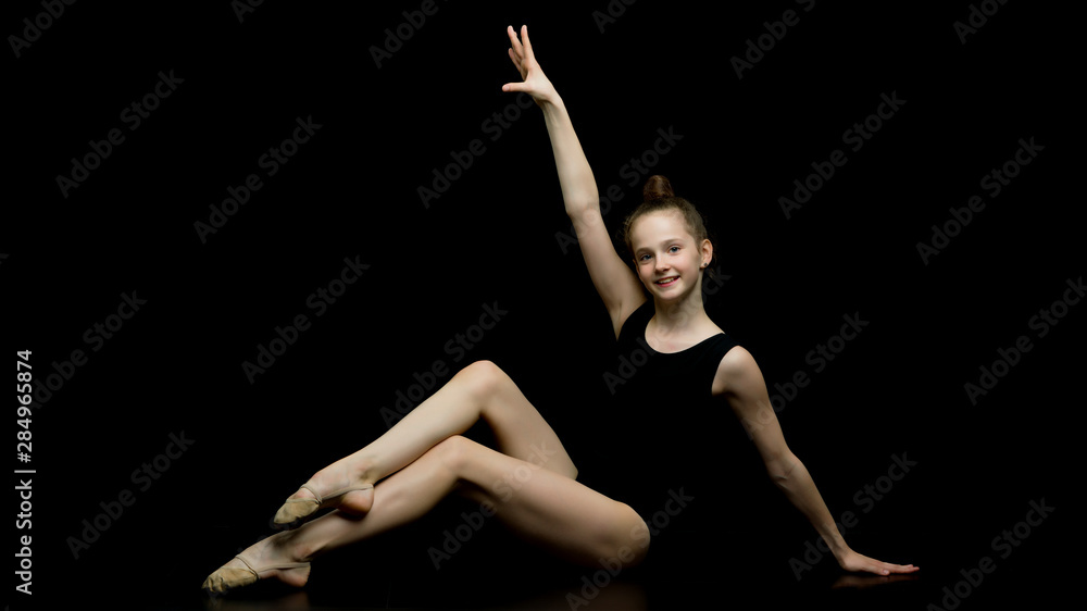 Girl gymnast in the studio on a black background performs gymnas