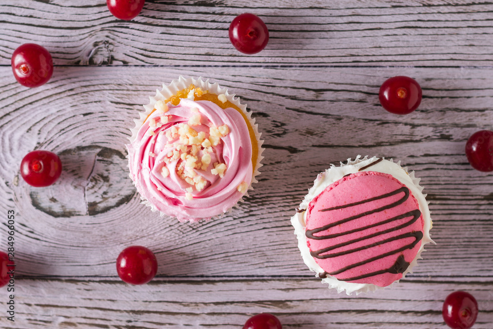 Ripe cherry berries and two cupcakes on a wooden table. Flat lay.