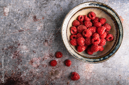 Top view of fresh raspberries in blue bowl on rust background with copy space. Still life concept.