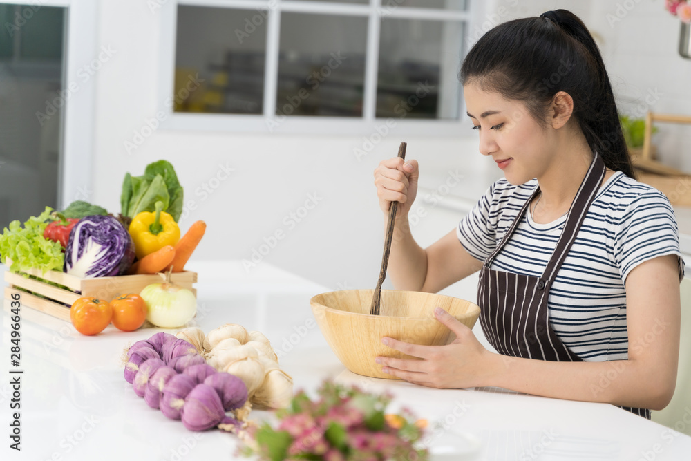 Asian young women are cooking healthy food Including vegetable salad in the bright white kitchen.