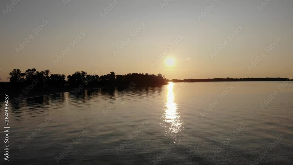 Slow flying drone at sunset over a large area of water with gentle waves and a beach Slow flying drone at sunset over a large area of water with gentle waves and a beach