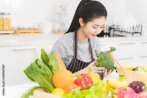 Beautiful asian woman is preparing to cook healthy food which consists of a variety of fruits and vegetables for the family. Housewife is smiling and holding broccoli. © amornchaijj