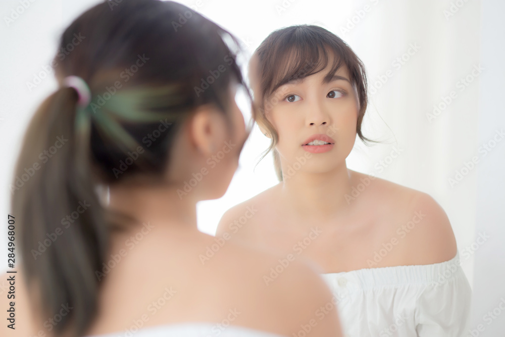 Beauty portrait young asian woman smiling look at mirror of checking skin care caucasian with wellness in the bedroom, beautiful girl happy touching face in reflection for health, lifestyle concept. Beauty portrait young asian woman smiling look at mirror of checking skin care caucasian with wellness in the bedroom, beautiful girl happy touching face in reflection for health, lifestyle concept.