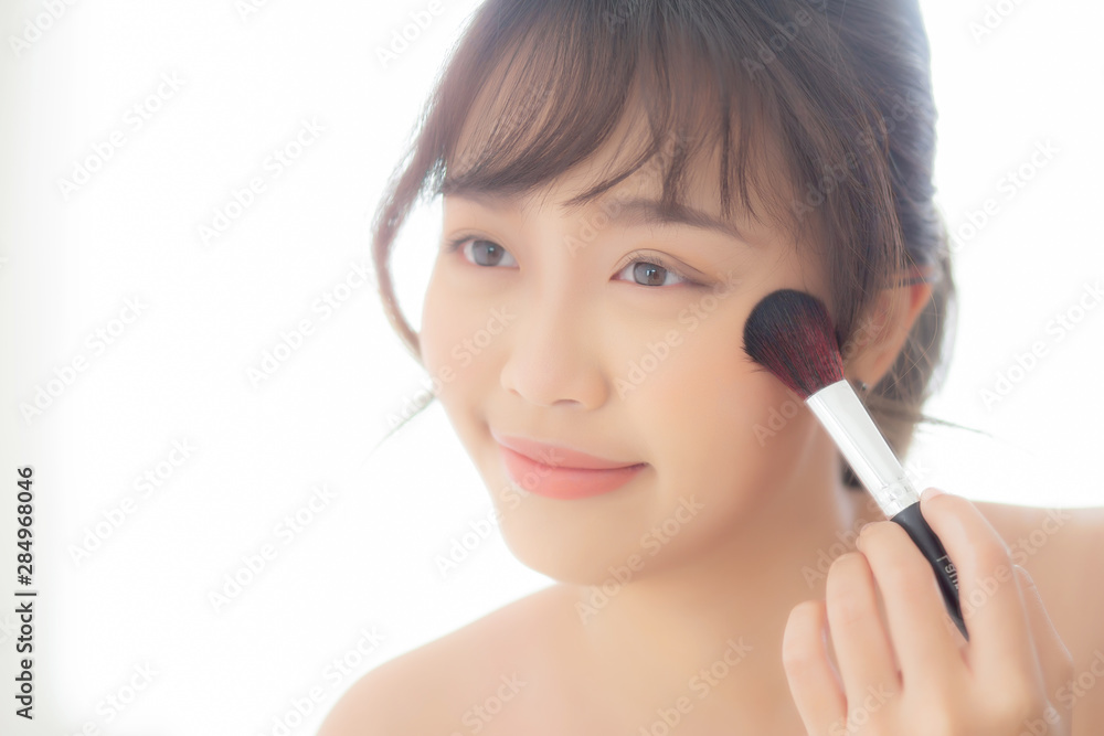 Beauty portrait young asian woman smile with face looking mirror applying makeup with brush cheek in the bedroom, beautiful of girl holding blusher, skin care and cosmetic concept. Beauty portrait young asian woman smile with face looking mirror applying makeup with brush cheek in the bedroom, beautiful of girl holding blusher, skin care and cosmetic concept.