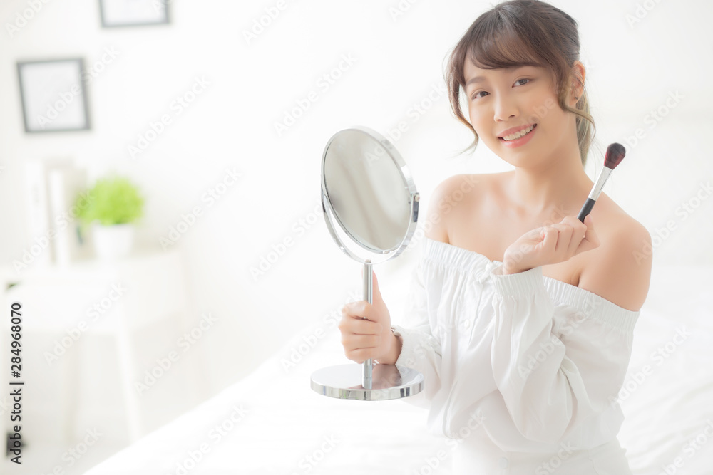 Beauty portrait young asian woman smile with face looking mirror applying makeup with brush cheek in the bedroom, beautiful of girl holding blusher, skin care and cosmetic concept. Beauty portrait young asian woman smile with face looking mirror applying makeup with brush cheek in the bedroom, beautiful of girl holding blusher, skin care and cosmetic concept.