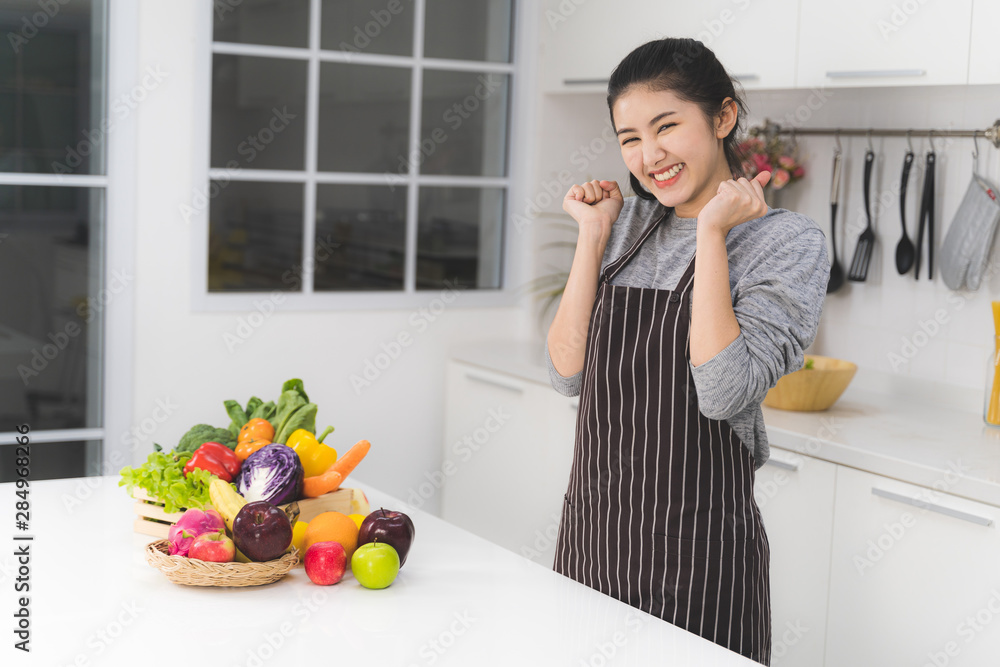 Portrait of beautiful asian woman, housewife is very happy in white kitchen with plenty of fresh vegetables and fruits on the table. Portrait of beautiful asian woman, housewife is very happy in white kitchen with plenty of fresh vegetables and fruits on the table.