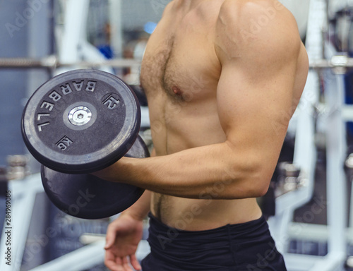 man with a naked torso holds a dumbbell in his hand, an athlete in the gym