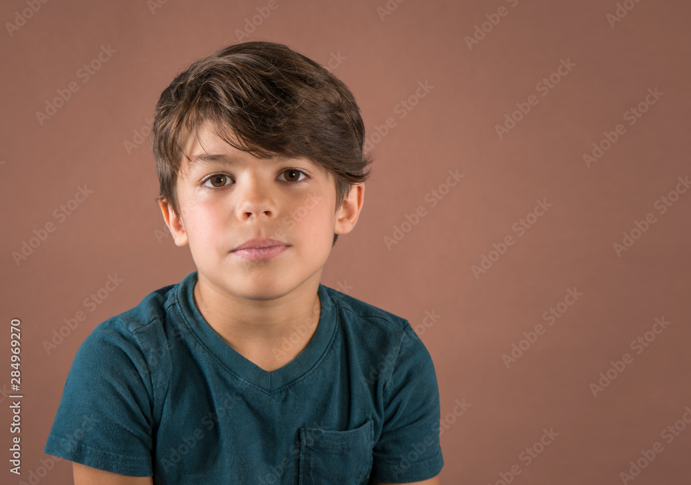 Handsome serious school age boy in teal t shirt looking at camera isolated on brown background Handsome serious school age boy in teal t shirt looking at camera isolated on brown background