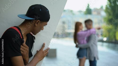 Disappointed african teenager looking female hugging classmate, unrequited love photo