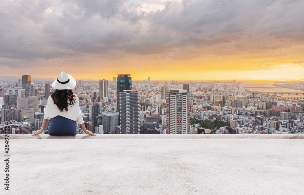 Φωτογραφία Woman in white hat sitting on building terrace, looking at city in sunset