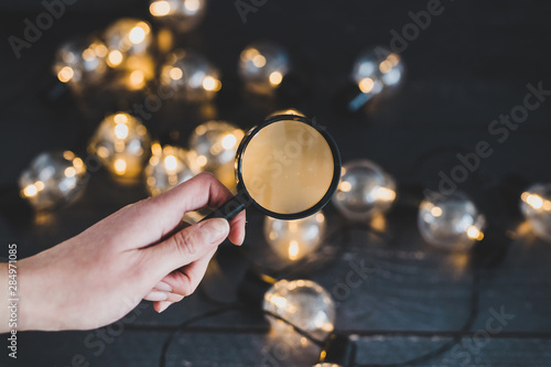hand holding magnifying glass analyzing different ideas in shape of lightbulb string lights photo