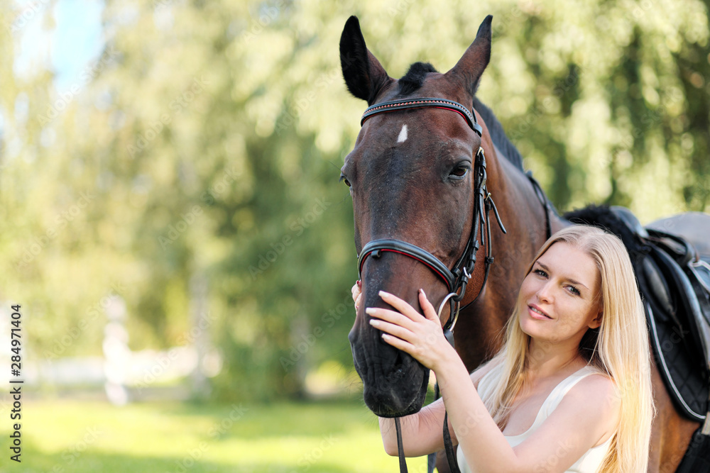 Obraz premium Young attractive blond woman hugs a brown horse.