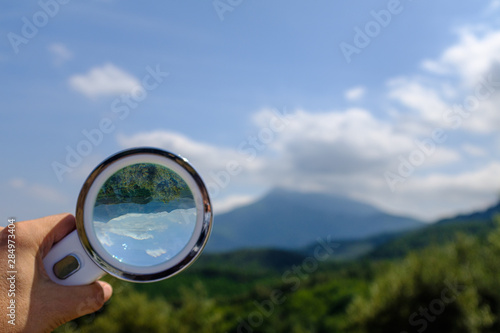 Handheld Loupe optical magnification effects view upside down on a green and blue nature landscape