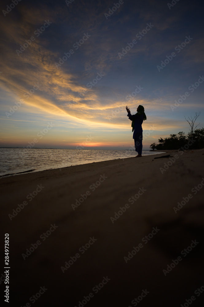 Muslim Girl saying prayer by the beach with sunset