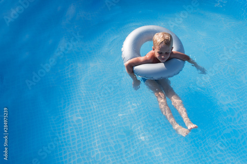 A boy with blond hair swims in a pool with blue water