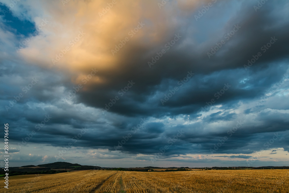 Blue cloudy dramatic sky with mowed field and hill, Czech republic