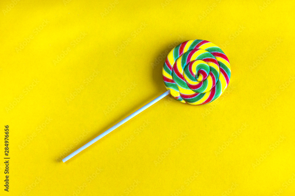 Multicolore lollipop swirl on wooden stick on a yellow background. Multicolore lollipop swirl on wooden stick on a yellow background.